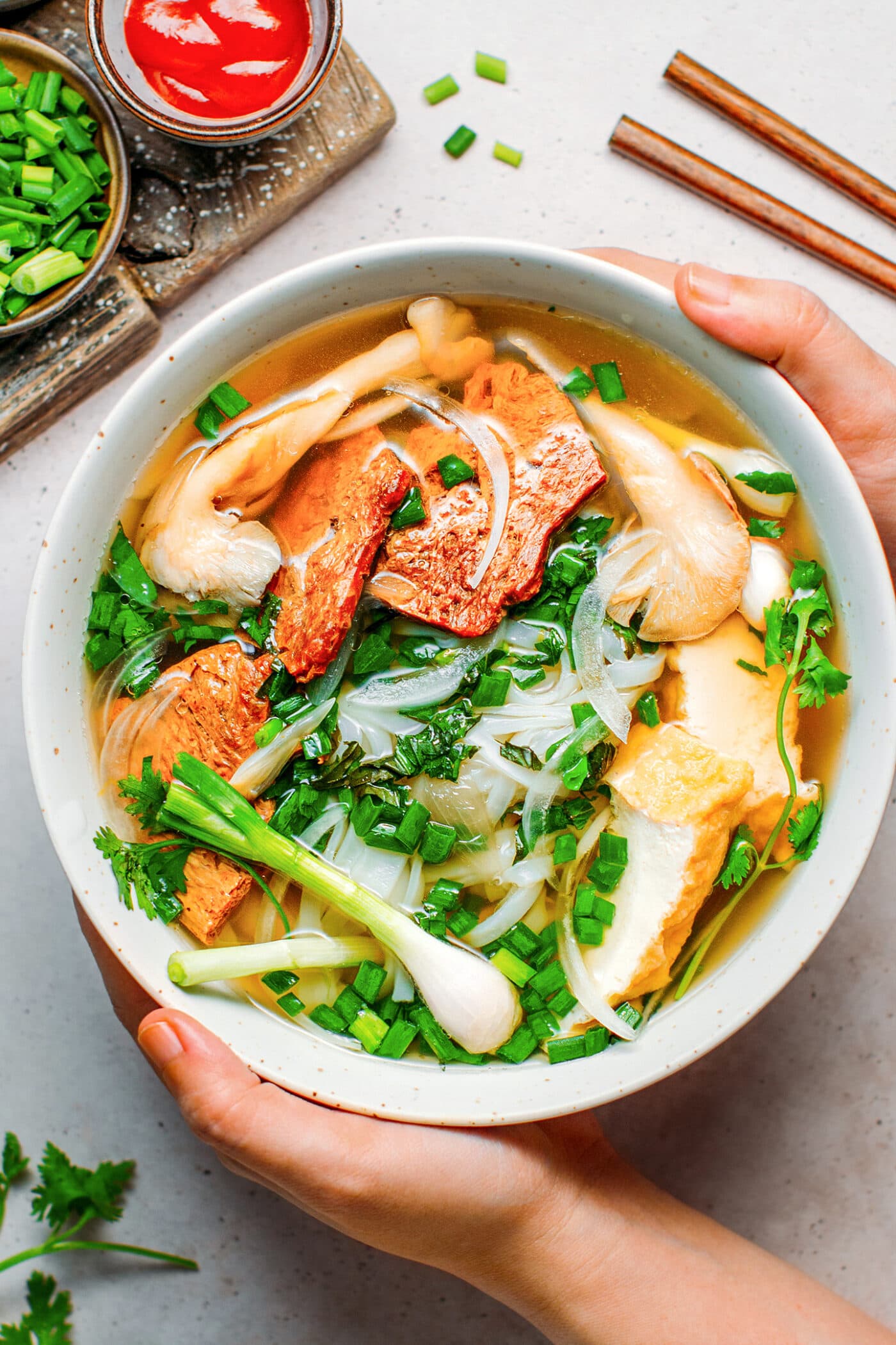 Bowl of vegan Pho with beef, tofu, mushrooms, and fresh herbs.