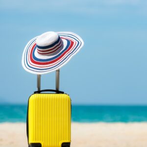 Holiday photo with suitcase and sun hat on a white beach with blue sky