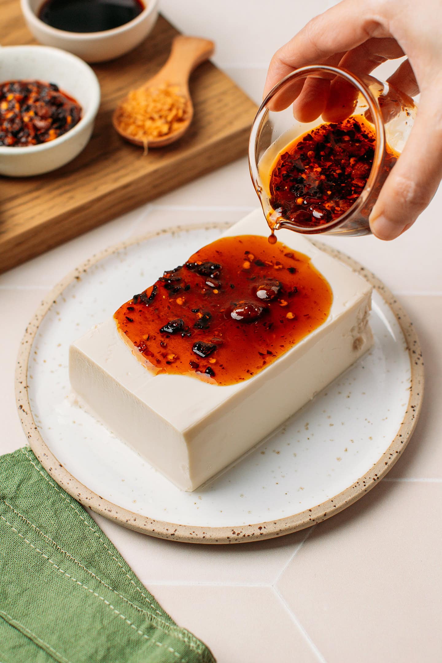 Pouring chili crisp sauce over a block of silken tofu.