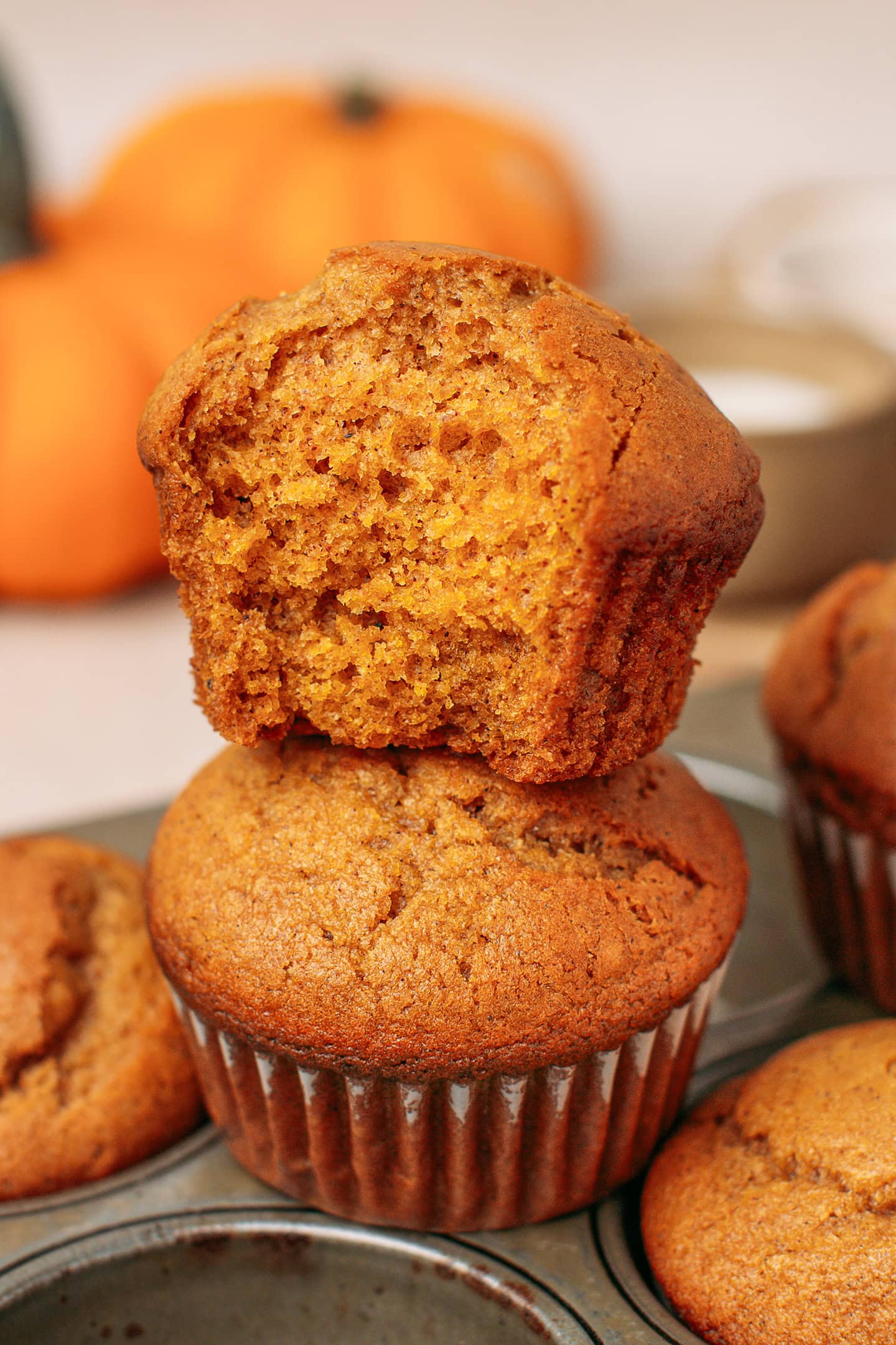 Two pumpkin muffins stacked on top of a muffin pan.